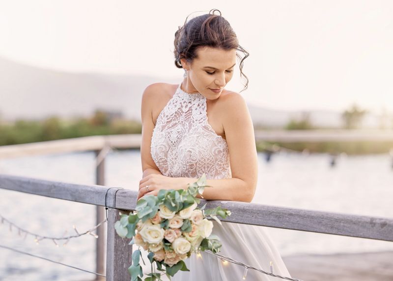 Wedding, bride fashion and flowers at lake for peaceful and classy outdoor marriage ceremony. Elegant, beautiful and stylish bridal woman with roses bouquet and white dress relaxing on pier.