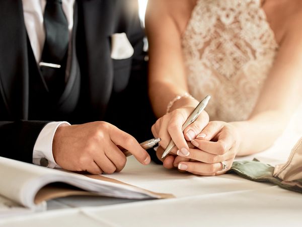 A couple in wedding attire holding pens, signing a document together.
