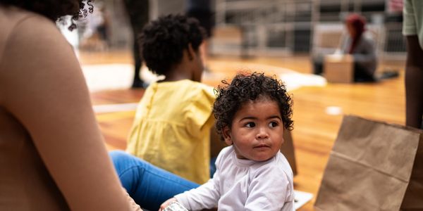 A toddler with curly hair sitting on the floor, looking to the side.