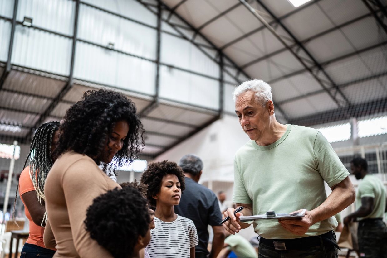Man with clipboard talking to a family indoors.
