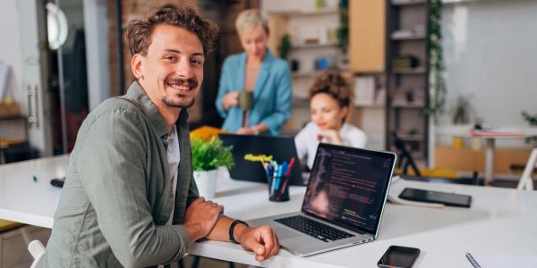Smiling man sitting with laptop in a modern office.