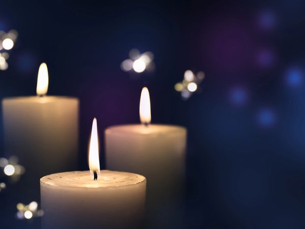 Three lit candles glowing softly against a dark, dreamy background with floating light orbs.