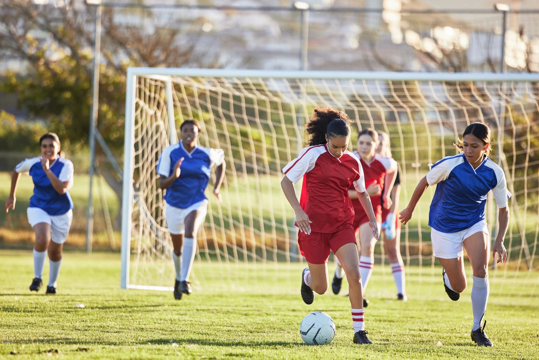 Girls playing soccer, chasing the ball.