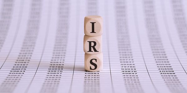 Wooden blocks spelling IRS on financial data sheets.