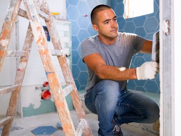A tile installer is working on a wall in a bathroom under renovation.