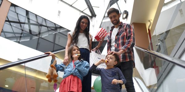 Family of four enjoying popcorn while standing on an escalator in a mall.