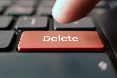 Finger about to press a red Delete key on a keyboard.