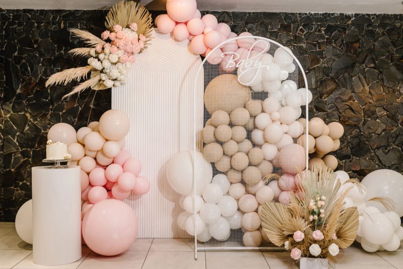 Birthday decorations - balloons, garland and decor for little baby party on a wall background. Celebration baptism concept. Baby text. Trendy Cake.