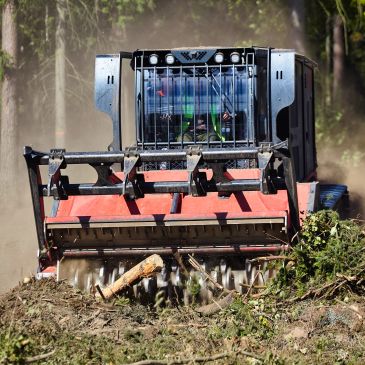Heavy machinery mulching tree branches and debris in a forest.
