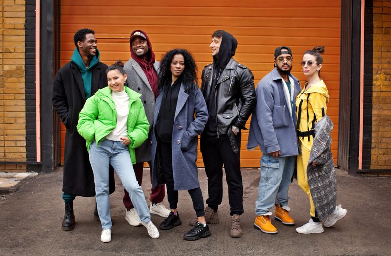 Multiracial group of young friends together on city street against orange colourful background. Diverse Stylish people outdoor, youth culture