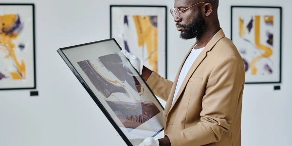 Man examining framed artwork in gallery.