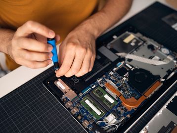 Hands repairing a laptop's internal hardware.