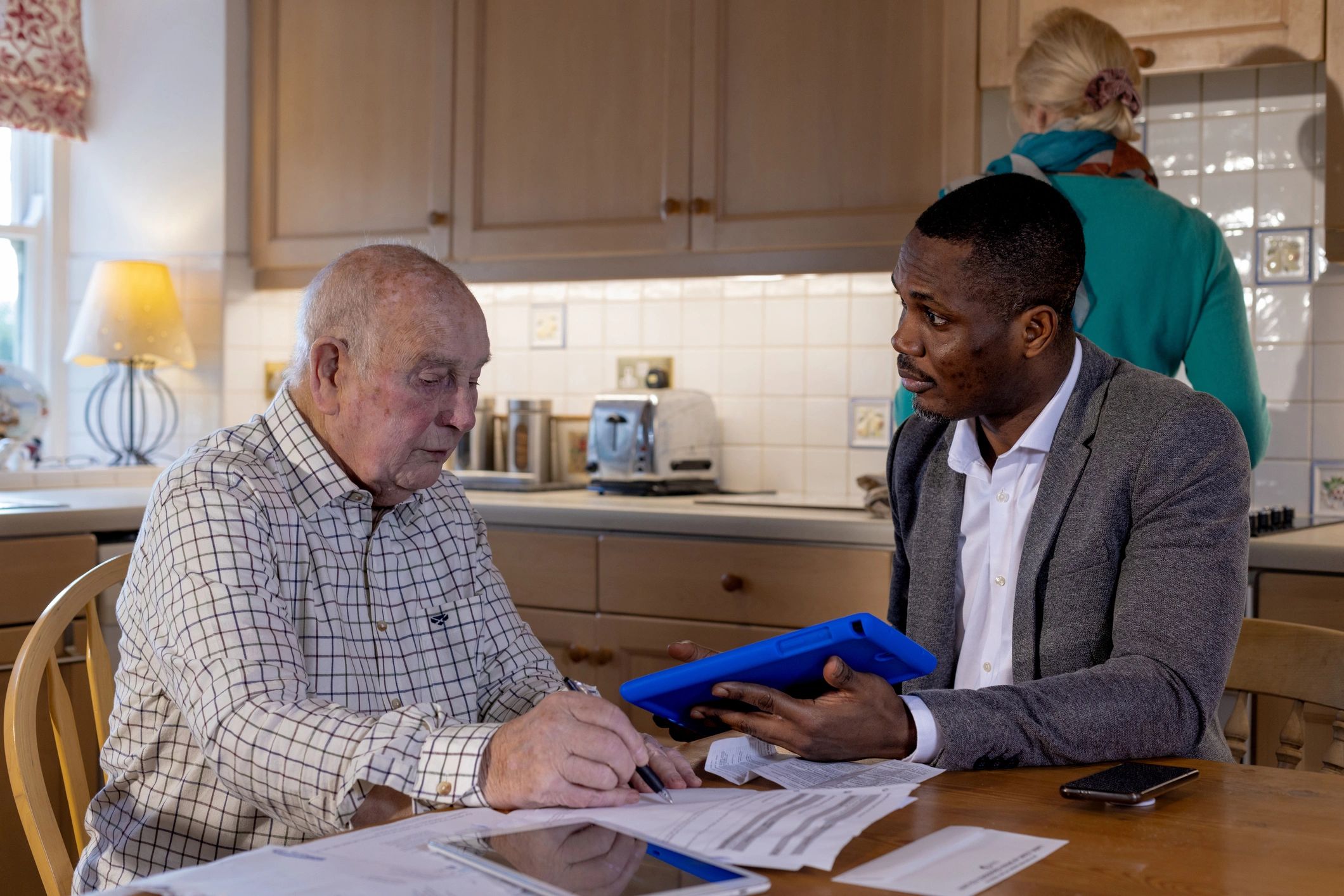 Black male professional assisting an older adult with paperwork during an in-home appointment.