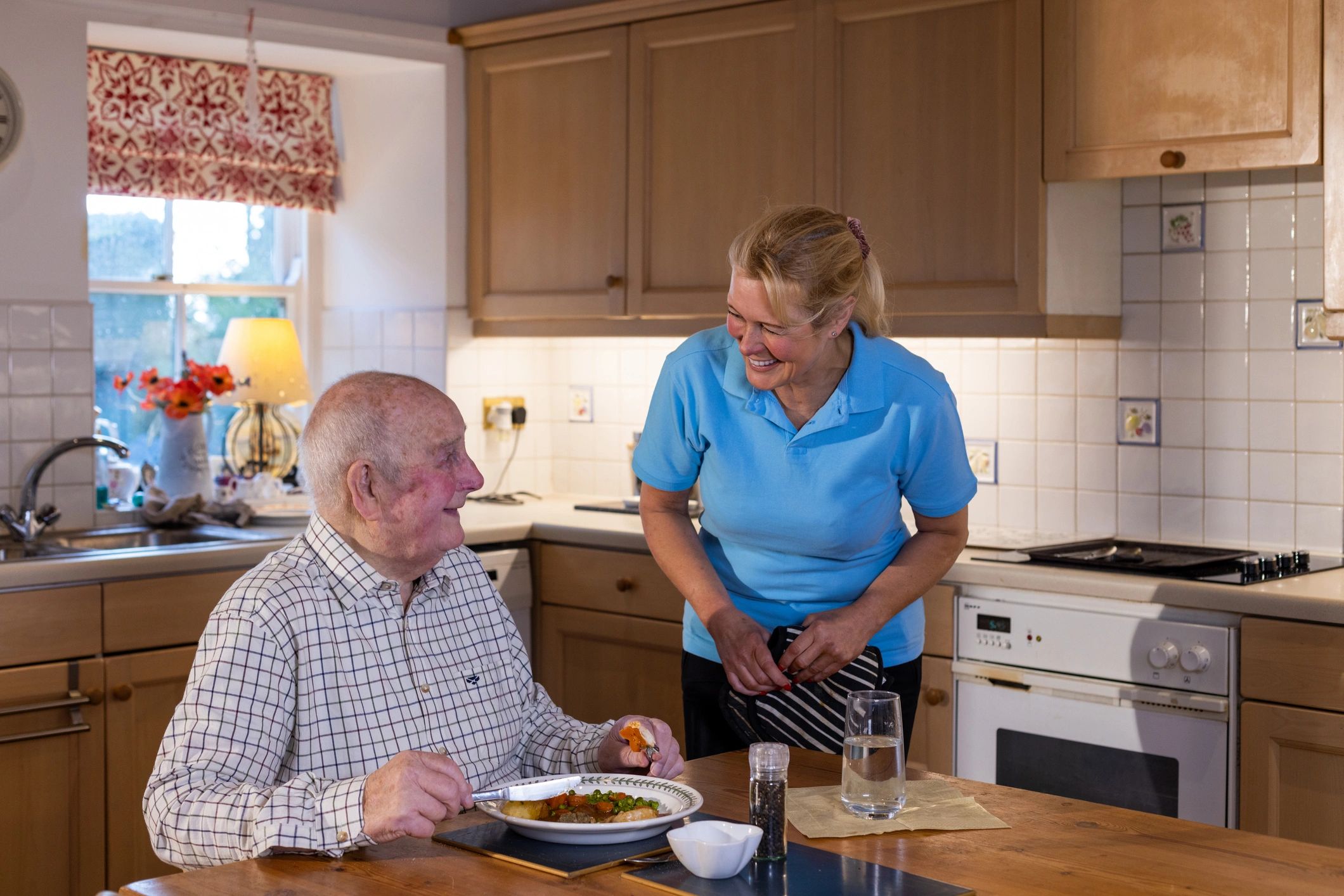 Caregiver smiling at elderly man having a meal in the kitchen.