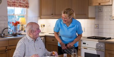 Caregiver smiling at elderly man during meal in a cozy kitchen.