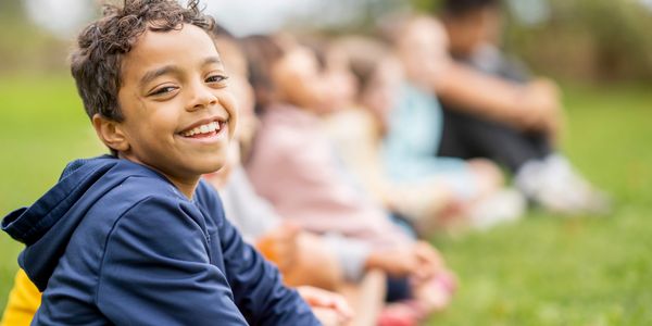 Happy boy in a blue hoodie sitting outdoors with friends in the background.