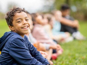 Smiling boy sitting on grass with friends in the background.
