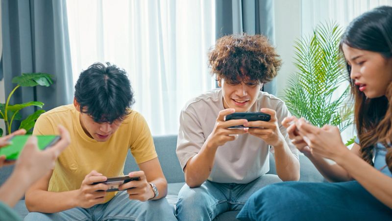 Happy group of Asian friends sitting on the sofa at home  having fun and playing  in smartphones,  Domestic Lifestyle with friend concept