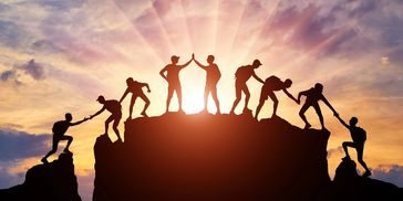 People helping each other climb a mountain at sunset.