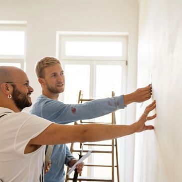 Two men examining and measuring a wall together in a bright room.