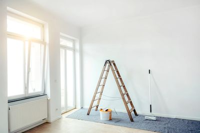 A bright room with painting tools and a wooden ladder set up.
