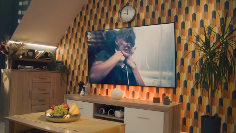 Couple sitting and hugging on sofa in cozy living room, watching action movie on TV or criminal blockbuster on streaming service, resting at home after workday. Home theater in modern apartment.
