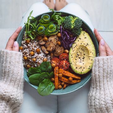 Colorful healthy bowl with avocado, veggies, and grains held in hands.