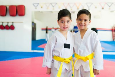 Two boys in white martial arts uniforms with yellow belts smiling in a dojo.