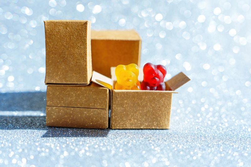 Two gummy bear candies peeping out of a shipping box isolated on a glittering background. Candy store party supplies concept.