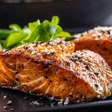 Grilled salmon fillet garnished with sesame seeds and fresh greens.