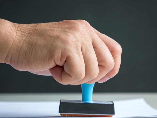 Hand pressing a blue stamp on paper with a dark background.