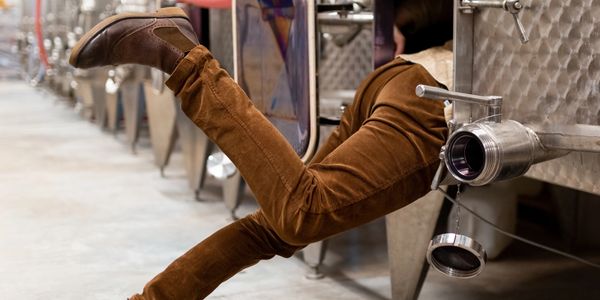 Person's legs sticking out from a metal tank in a brewery or winery.