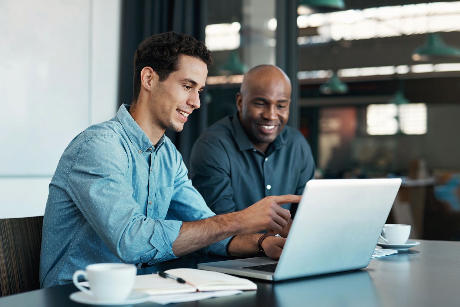 Two men collaborating and smiling while working on a laptop.