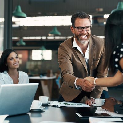 Business meeting with a friendly handshake and smiles around the table for staffing and recruitment.
