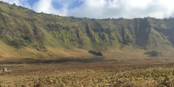 Vast dry field with tall green cliffs under a partly cloudy sky.