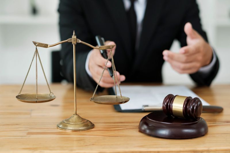 Attorney of lawyer discussing and consulting client about his offense, explaining cases, giving advise for going to courtroom with judge gavel and scale of justice on the table.