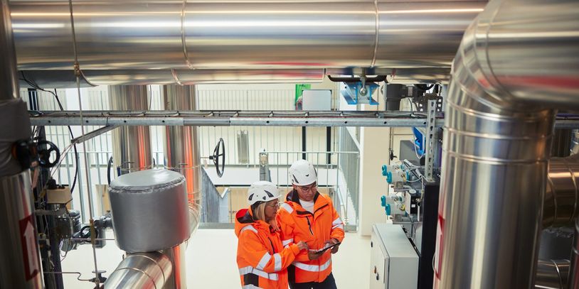 Two engineers inspect industrial machinery in a plant wearing safety gear.