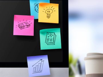 Sticky notes with business icons on a computer monitor.