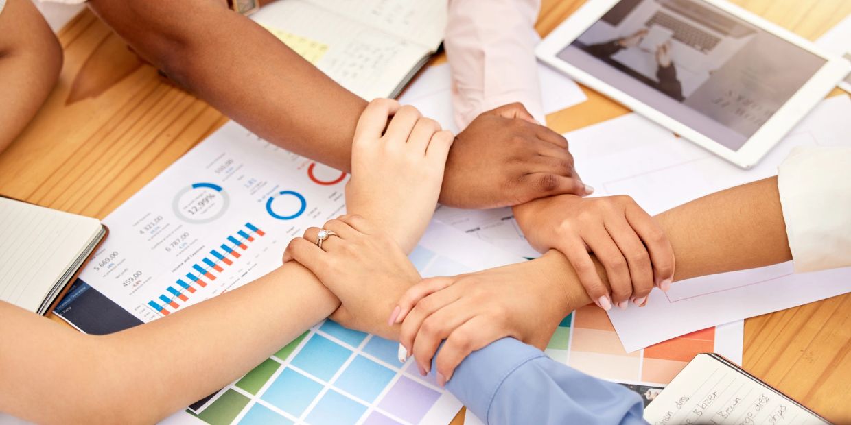 Team members joining hands in unity over work documents.