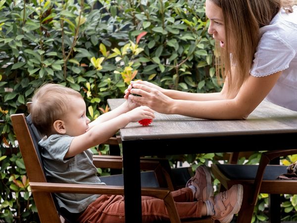 Woman playfully interacts with toddler at a table outdoors.