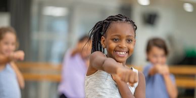 Smiling girl practicing martial arts with others in the background.