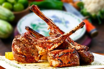 Grilled lamb chops plated with herbs and a side of corn.