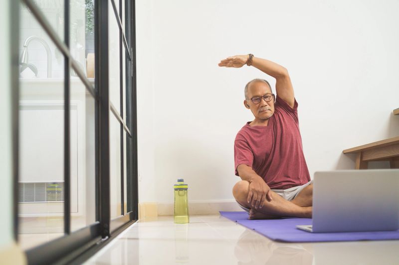 Asian senior Adult man training and stretching arm with Laptop, Home Workout exercises, Healthy lifestyle concept