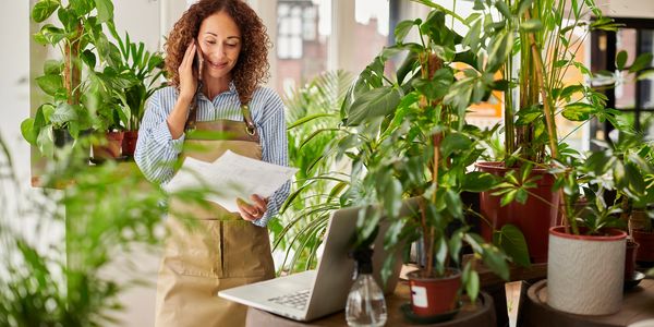 Woman in apron talking on phone and checking papers in a plant shop.