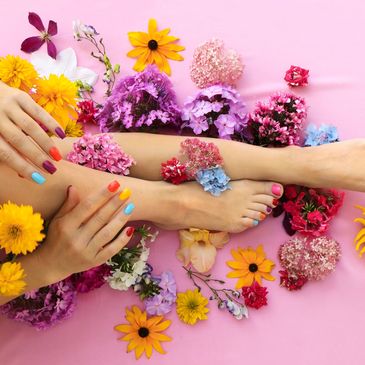 Colorful painted nails and toes surrounded by vibrant flowers on a pink background.