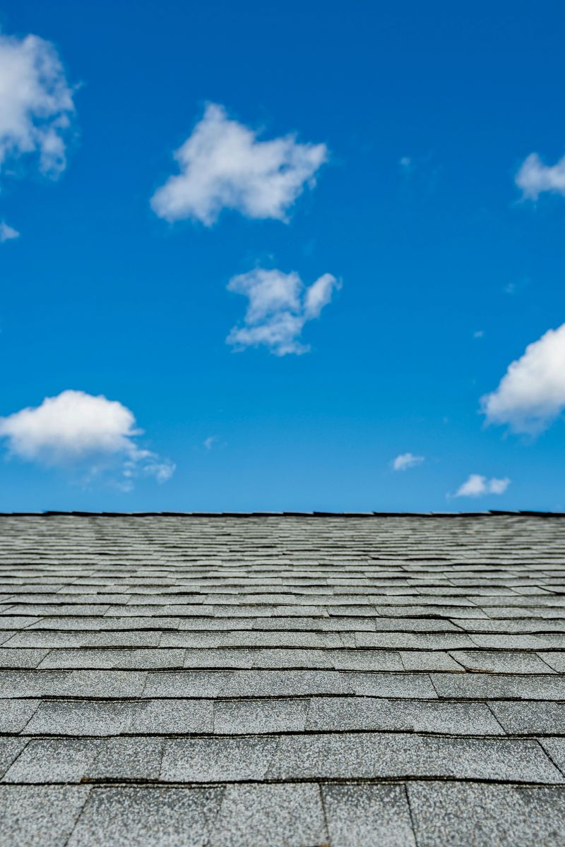 Newly installed gray architectural asphalt shingles on a residential house during a remodeling project, with blue sky and puffy clouds in background.
