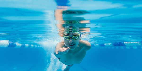 Boy swimming underwater in a pool wearing goggles.