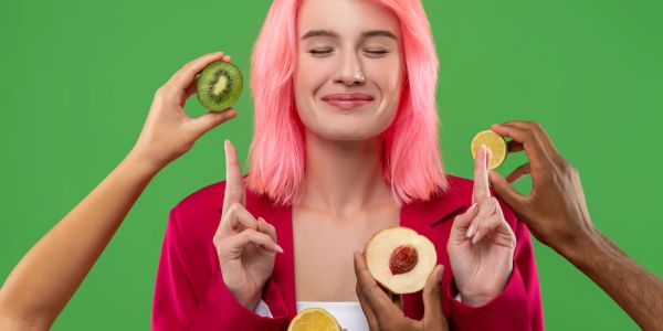 Woman with pink hair surrounded by hands holding fruits.