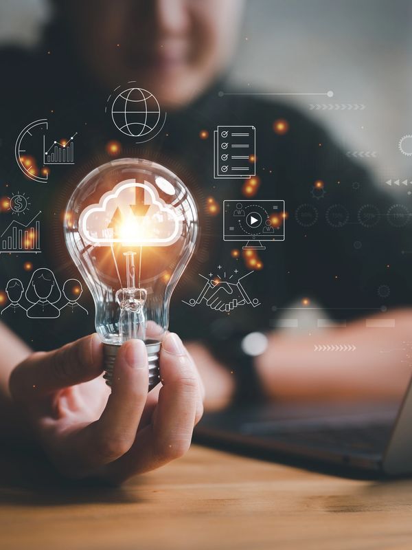Person holding a light bulb with digital cloud and technology icons around it.