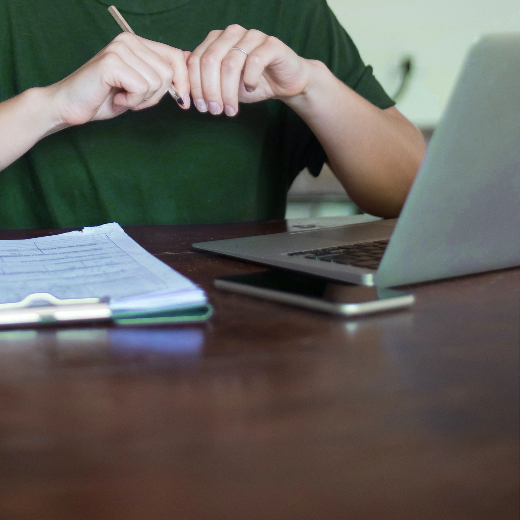 Person holding a pencil near a laptop and documents on a desk.